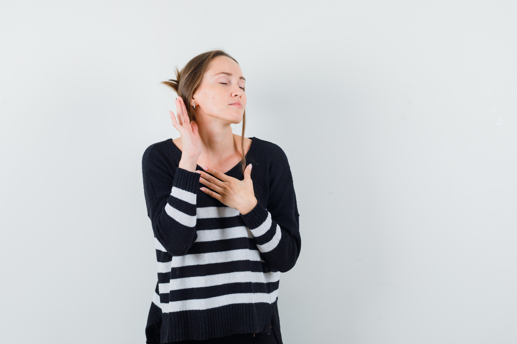 young-woman-standing-listening-pose-holding-one-hand-chest-while-closing-eyes-striped-knitwear-black-pants-looking-happy-2-_main